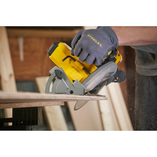 STANLEY SFMCS500M2K cordless circular saw cutting wood, side angle, with branded work glove.