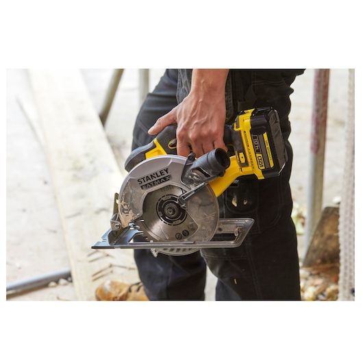 STANLEY SFMCS500M2K cordless circular saw held by worker, yellow and silver, construction setting.