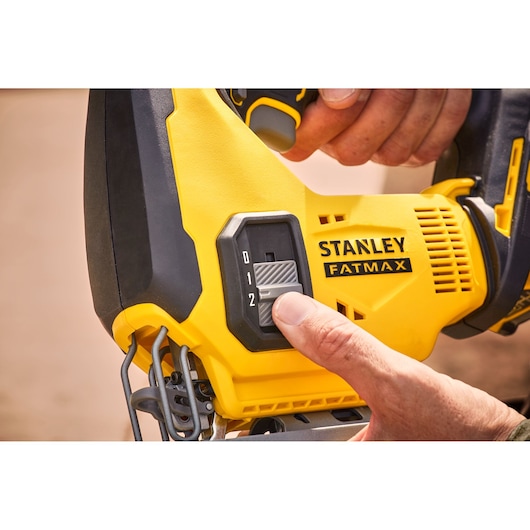 Stanley SFMCS600D1K jigsaw, close-up of speed control switch, yellow and black handle, hand adjusting.