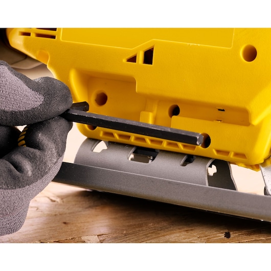 STANLEY SFMCS600D1K jigsaw close-up, gloved hand adjusting base angle with hex key on wooden surface.
