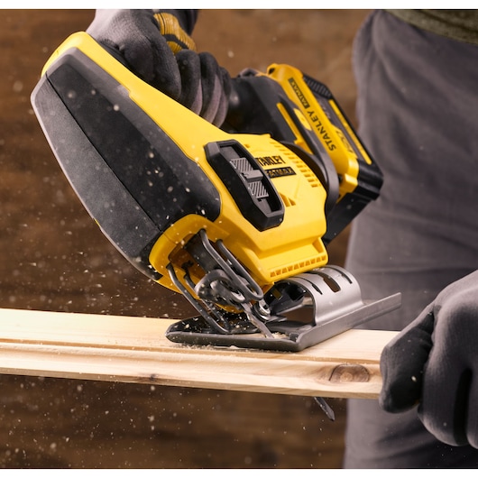 STANLEY SFMCS600M1K cordless jigsaw cutting wood, close-up view with sawdust particles in action.