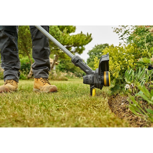 STANLEY SFMCST925M1 grass trimmer in use trimming lawn edge, close-up outdoor view.