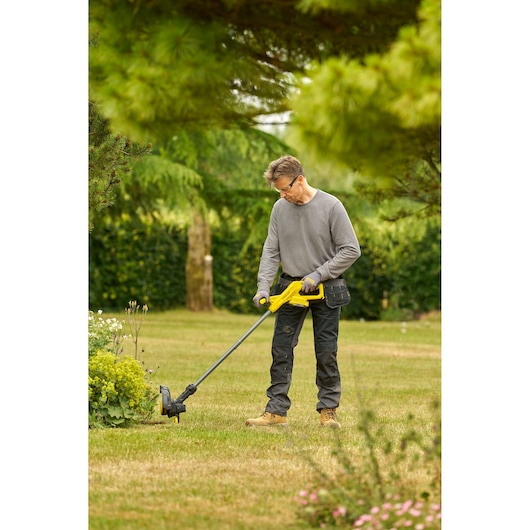 STANLEY SFMCST925M1 yellow cordless grass trimmer in use outdoors on lawn, product photography.