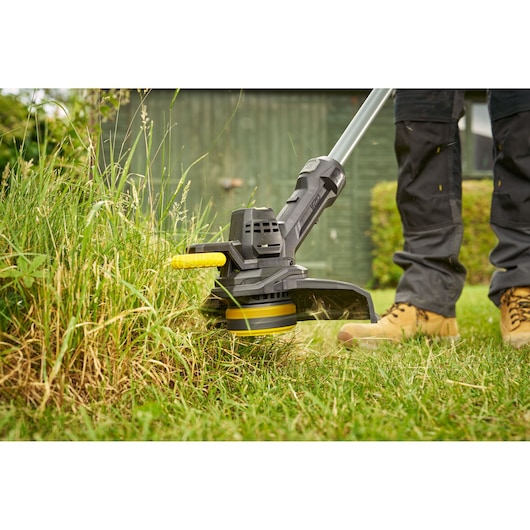 STANLEY SFMCST925M1 grass trimmer in use, close-up of cutting head trimming tall grass outdoors.