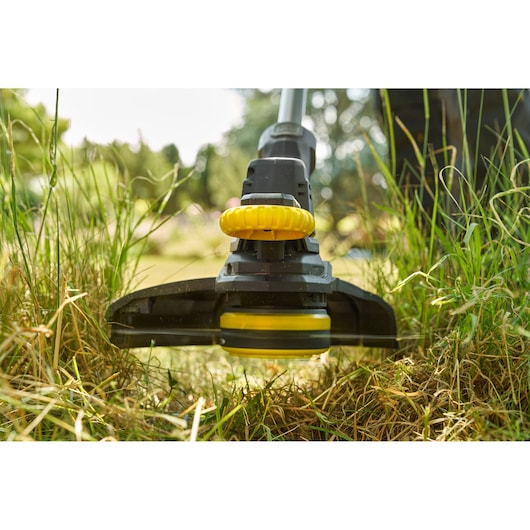 STANLEY SFMCST925M1 grass trimmer close-up trimming lawn, showing yellow and black head outdoors.