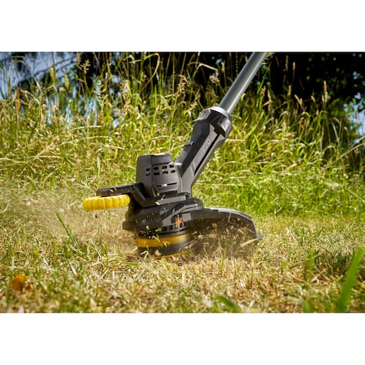STANLEY SFMCST925M1 grass trimmer close-up cutting tall grass outdoors.