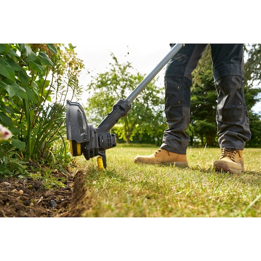 STANLEY SFMCST925M1 grass trimmer in use edging a garden lawn, close-up outdoor photography.