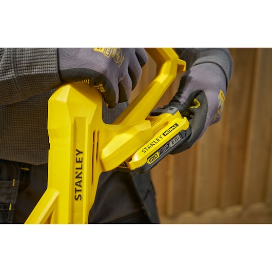 STANLEY SFMCST925M1 yellow cordless tool close-up, gloved hands inserting V20 battery.