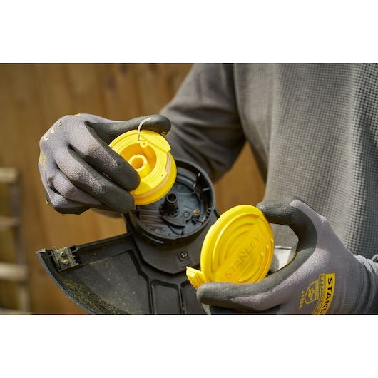STANLEY SFMCST925M1 spool replacement for string trimmer, close-up with yellow parts and gloves.