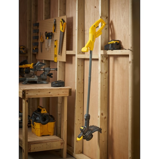 STANLEY SFMCST925M1 cordless string trimmer in yellow and black, side view, hanging in a workshop.