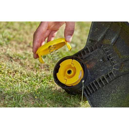 STANLEY SFMCST933M1 grass trimmer spool assembly close-up on lawn, yellow cap and spring detail.