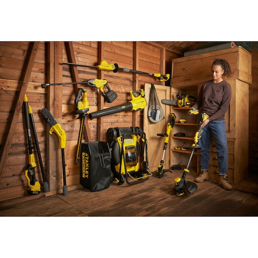 STANLEY SFMCST933M1 garden tools and accessories in shed, yellow and black, person holding string trimmer.