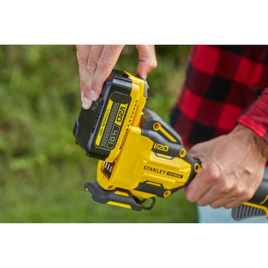 Stanley SFMCSTB933M V20 yellow cordless tool, close-up of battery installation outdoors.