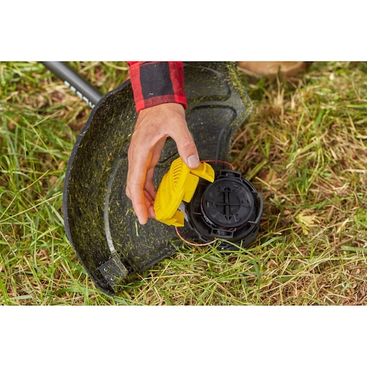 STANLEY SFMCSTB933M grass trimmer head close-up, hand installing yellow part, outdoor setting.