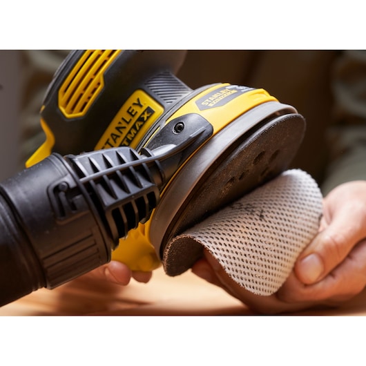 Photo of STANLEY SFMCW220M1S sander with sanding pad held by hand, close-up view.