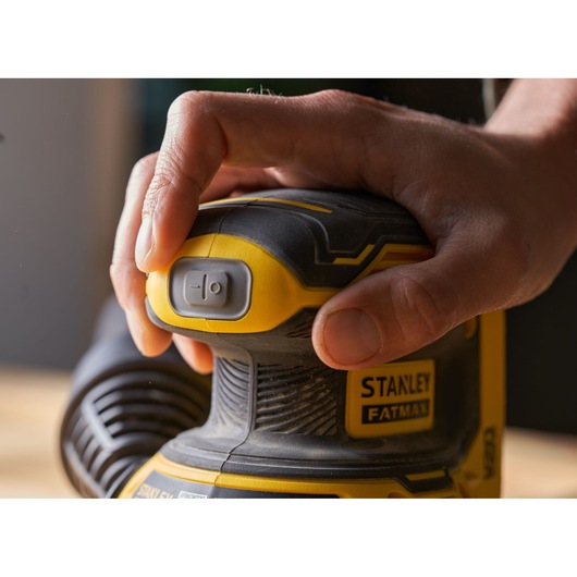Photo of STANLEY SFMCW220M1S sander being switched on, close-up of hand pressing power button, yellow and black design.