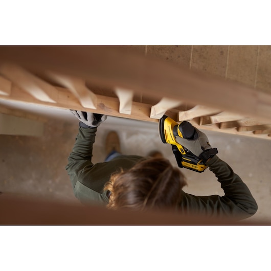 Photo of person using STANLEY SFMCW221D1S cordless sander on wooden railing, wearing gloves.