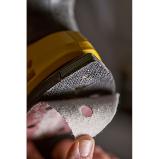 STANLEY SFMCW221D1S sander close-up with sanding pad being attached, showing yellow and black tool body.