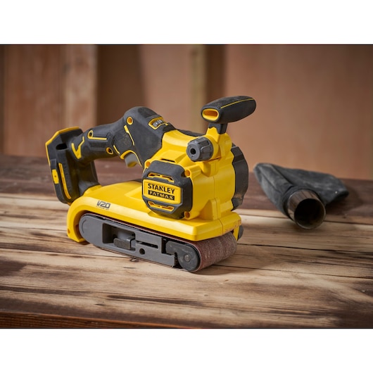 STANLEY SFMCW223B-XJ belt sander, yellow and black, side angle, on wooden surface.