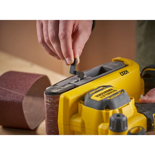 Close-up of STANLEY SFMCW223B-XJ belt sander in use with a hand adjusting the sanding belt, product photography.