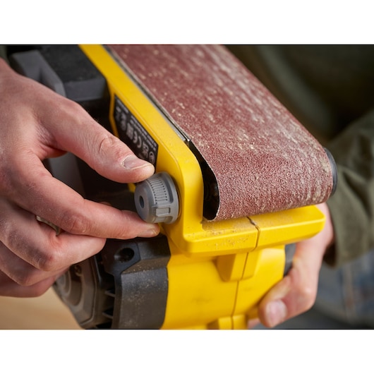 STANLEY SFMCW223B-XJ belt sander close-up, yellow body, sanding belt adjustment knob.