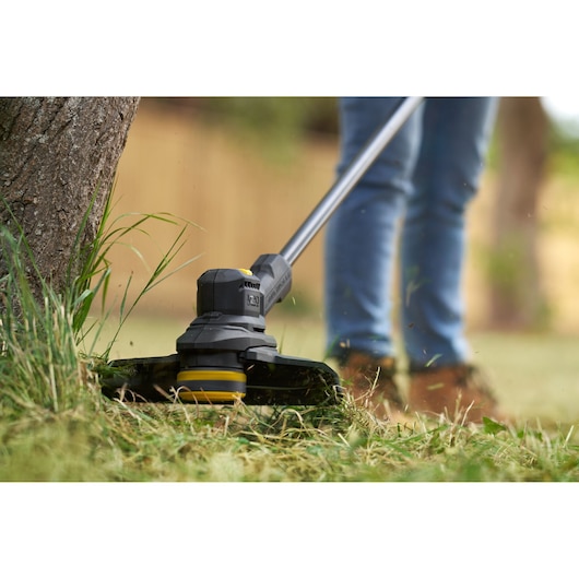 STANLEY SFMSTB930M grass trimmer close-up in use, cutting grass around a tree in a garden.