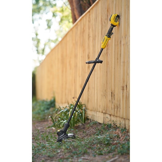 STANLEY SFMSTB930M grass trimmer in yellow and black leaning against a wooden fence outdoors.