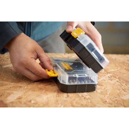 Photo of STANLEY STA88560 small parts organizer with clear lid, yellow latch, and black base being opened on a wooden surface.