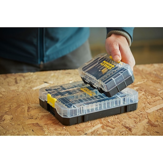 STANLEY STA88560 organizer box with clear lid, yellow latch, shown on wood surface held by hand.