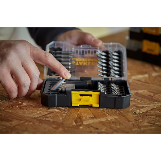 STANLEY STA88560 drill bit set case with yellow latch, person selects a bit, close-up on wooden surface.