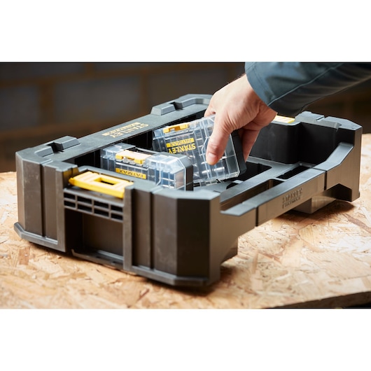 STANLEY STA88560 organizer box with clear compartments and yellow latches, hand placing container inside, front angle.