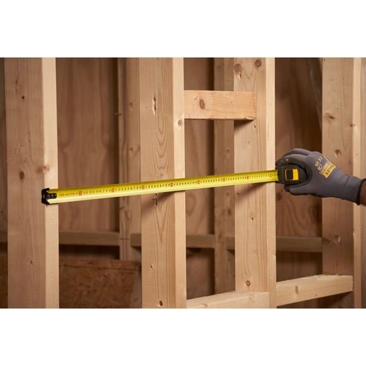 STANLEY STHT0-33561 tape measure in use measuring wooden studs, workshop setting, side view.