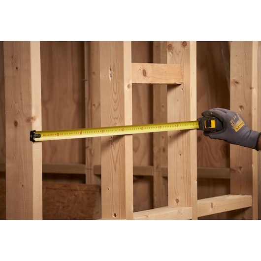 STANLEY STHT0-33566 tape measure in use measuring wooden studs at a construction site.