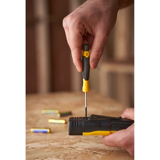 STANLEY STHT0-62144 screwdriver in use on black and yellow device, close-up on wooden surface with batteries.