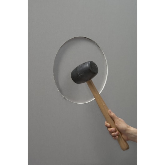 STANLEY STHT1-05878 rubber mallet with wooden handle, side view, held against a gray wall with a circular cutout.