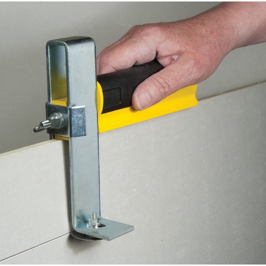 STANLEY STHT1-16069 metal and yellow drywall carrier tool in use on a drywall sheet, close-up side view.