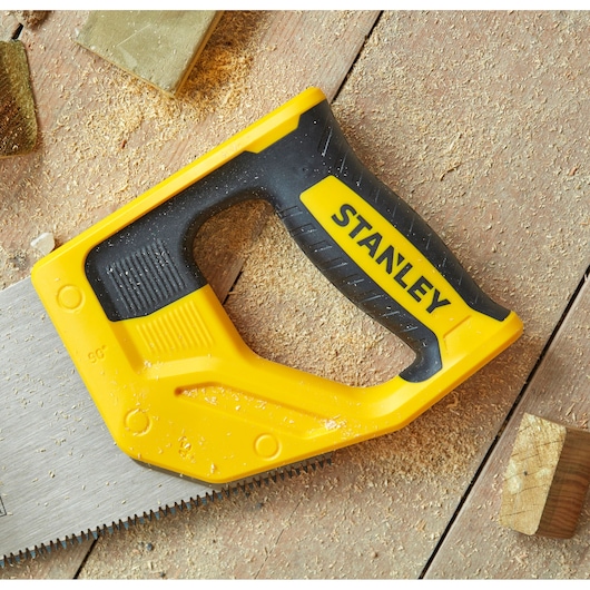 STANLEY STHT1-20353 handsaw with yellow and black ergonomic handle on wood surface with sawdust.