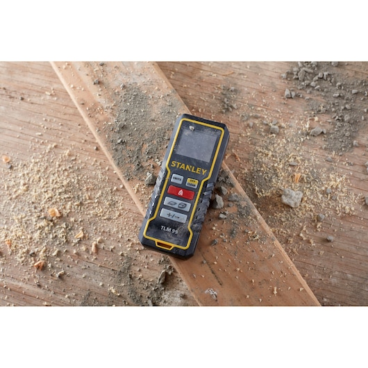 STANLEY STHT1-77138 laser distance measurer on dusty wood surface, angled view.