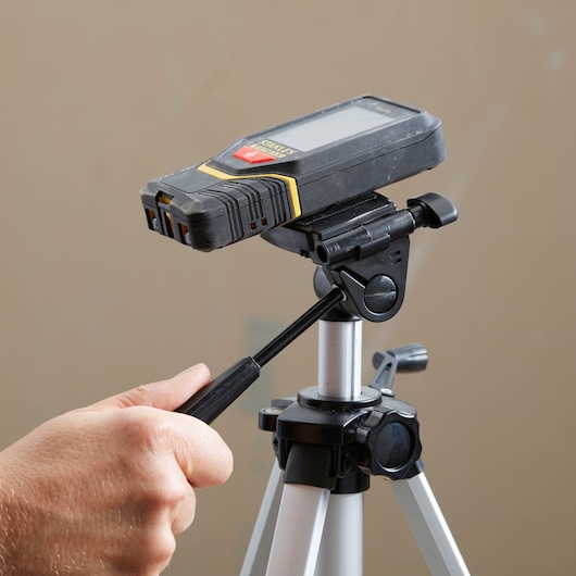 STANLEY STHT1-77140 digital laser measure on tripod, hand adjusting mount lever, close-up.