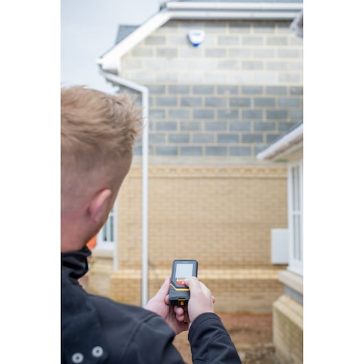 Photo of a person using a STANLEY STHT1-77140 laser distance measurer outside near a brick building.