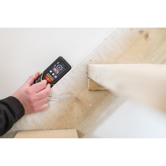 STANLEY STHT1-77140 distance measurer in use against a wall by a hand, close-up angle.