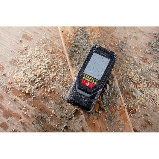 STANLEY STHT1-77142 rugged laser distance measurer with water droplets on screen, placed on dirty wood surface.