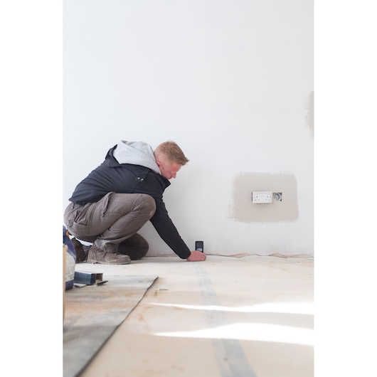 Person using STANLEY STHT1-77142 laser distance measurer on wall in construction setting.