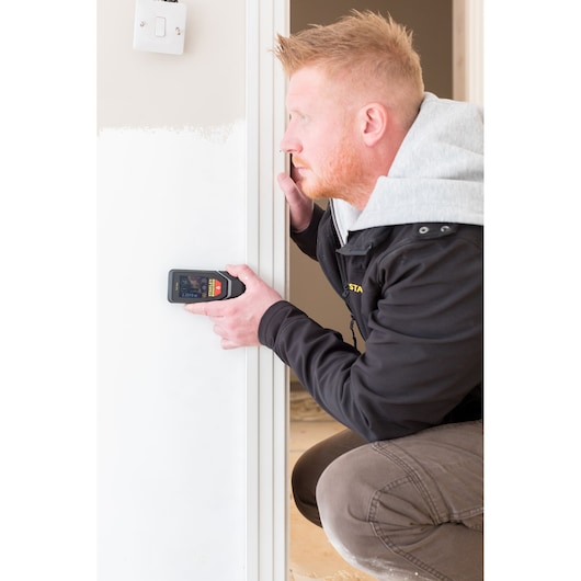 Person using STANLEY STHT1-77142 electronic detector on white interior wall, close-up view.