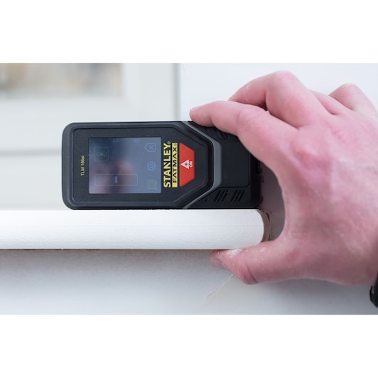 Photo of STANLEY STHT1-77142 laser measuring device held against a white wall.