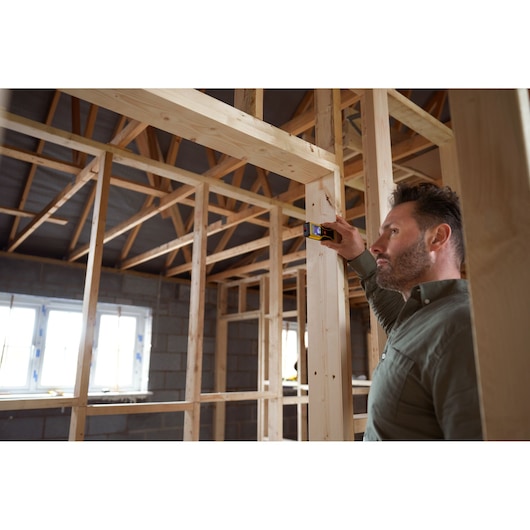 STANLEY STHT1-77409 laser distance measurer used by person measuring wooden frame in unfinished building.