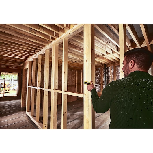STANLEY STHT1-77409 laser distance measurer in use at wooden house construction site.