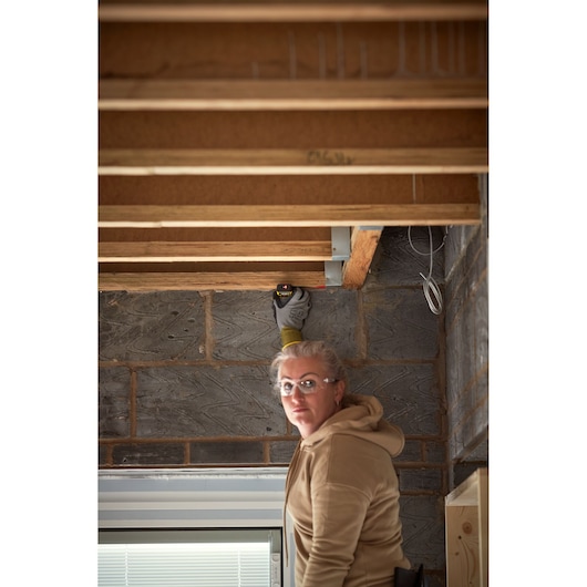 Photo of STANLEY STHT1-77409 laser distance measurer in use on exposed ceiling beams at construction site.