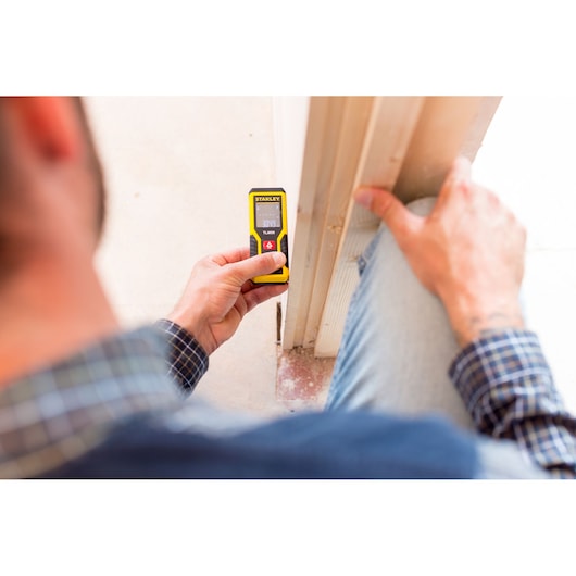 Photo of a person using a STANLEY STHT1-77409 laser distance measurer against a door frame.