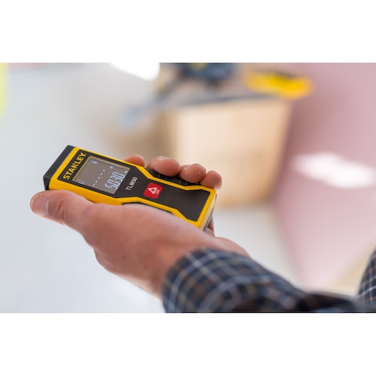 STANLEY STHT1-77409 laser distance measurer held in hand, close-up photography in indoor setting.